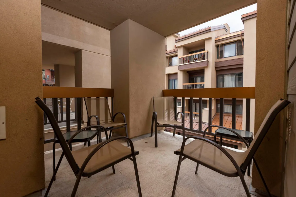 This image features four outdoor chairs arranged in a conversational grouping on a balcony, with wooden railings and views of adjacent building facades. The scene encourages relaxed conversation and connection, set in fresh mountain air.